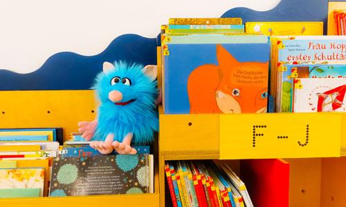 Kinderbücher in einem Regal, auf dem eine Spielzeugfigur sitzt