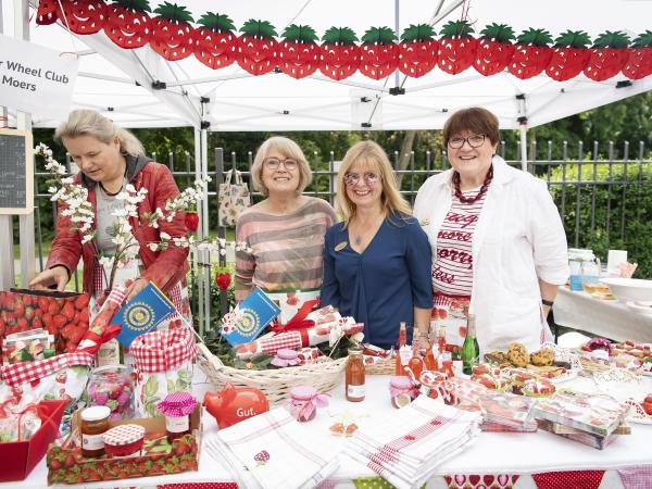 Vier Frauen am Stand des Inner Wheel Club Moers, der mit dem Thema Erdbeeren dekoriert ist.