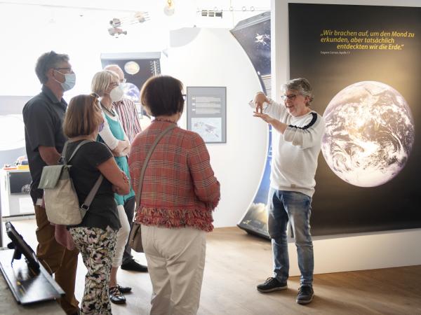 Ein Mann erklärt einer Gruppe von Personen etwas über eine Ausstellung im Museum.