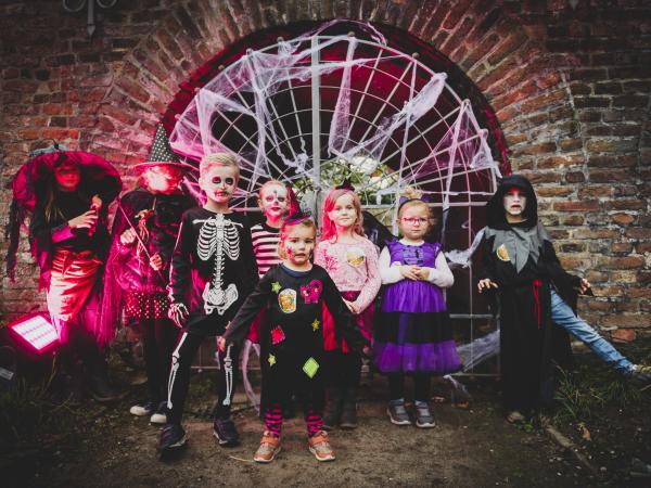 Mehrere kostümierte Kinder stehen vor einem Tor mit Spinnenweben.