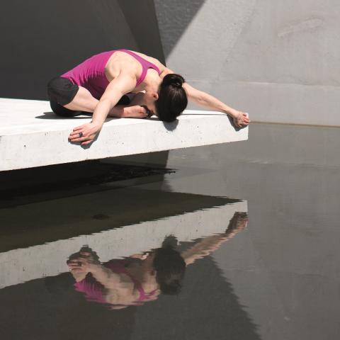 Ein Frau in Yoga-Pose, die sich im Wasser spiegelt.