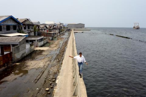 Eine heruntergekommene Wohnsiedlung am Meer und eine Person läuft am Wasser entlang.