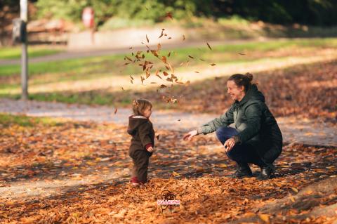 Eine Frau und ein Kleinkind spielen mit Laub.